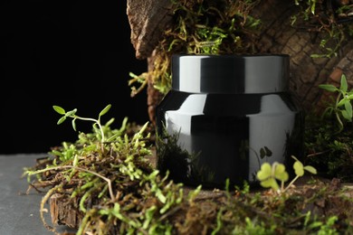 Photo of Jar of moisturizing body cream, tree bark and plants on grey table, closeup. Space for text