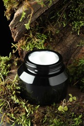 Photo of Jar of moisturizing body cream on tree bark with plants, closeup