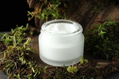 Photo of Jar of moisturizing body cream on tree bark with plants, closeup