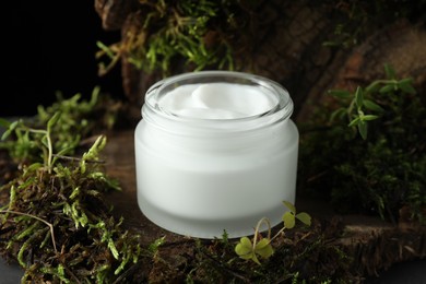 Photo of Jar of moisturizing body cream on tree bark with plants, closeup