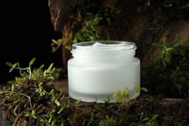 Photo of Jar of moisturizing body cream on tree bark with plants, closeup