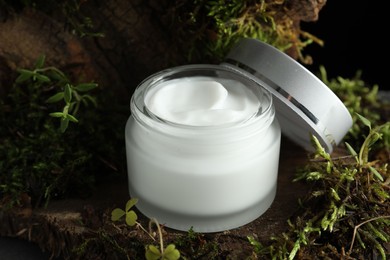 Photo of Jar of moisturizing body cream on tree bark with plants, closeup