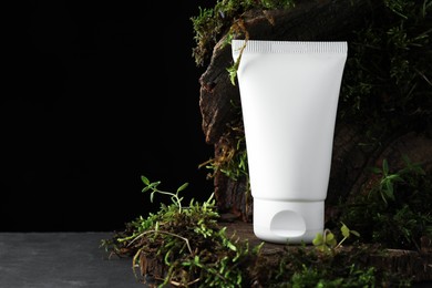 Photo of Tube of moisturizing body cream, tree bark and plants on grey table, closeup. Space for text
