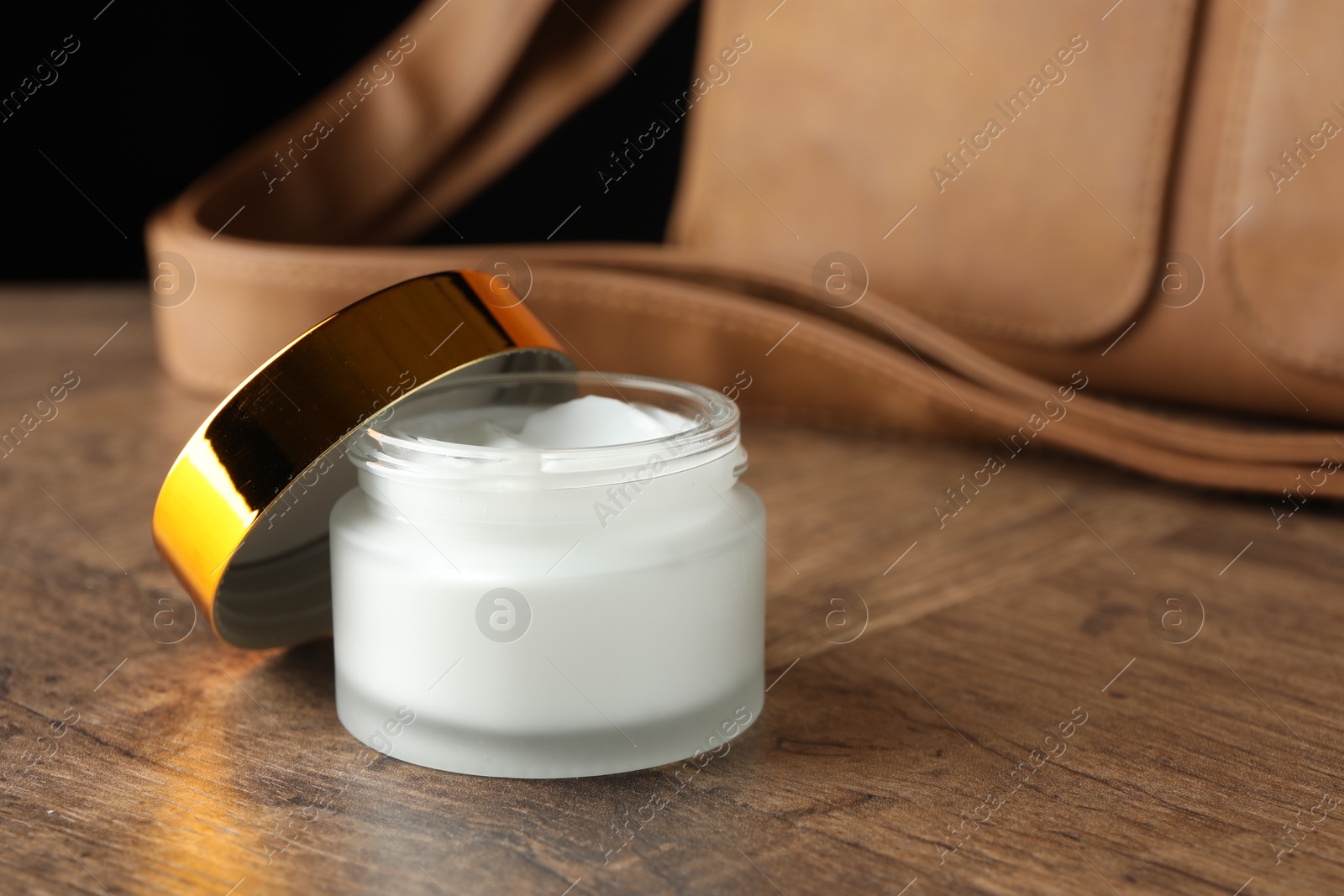 Jar of moisturizing body cream and leather bag on wooden table, closeup. Space for text Photo of Jar of moisturizing body cream and leather bag on wooden table, closeup. Space for text