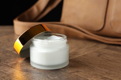 Photo of Jar of moisturizing body cream and leather bag on wooden table, closeup. Space for text