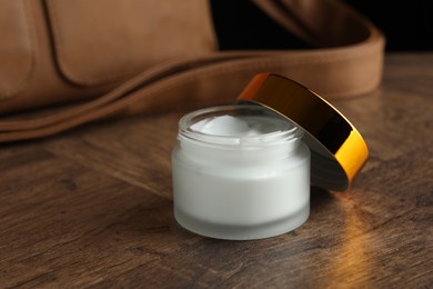 Photo of Jar of moisturizing body cream and leather bag on wooden table, closeup