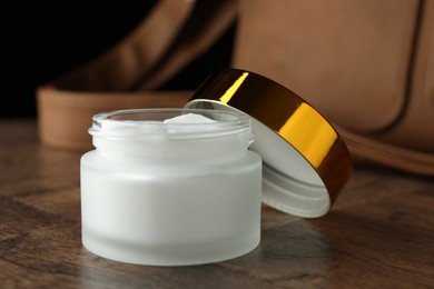 Photo of Jar of moisturizing body cream and leather bag on wooden table, closeup