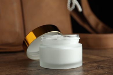 Photo of Jar of moisturizing body cream and leather bag on wooden table, closeup