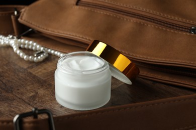 Photo of Jar of moisturizing body cream and leather bag on wooden table, closeup