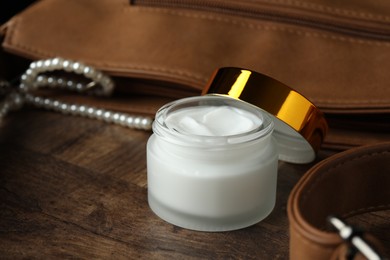 Photo of Jar of moisturizing body cream and leather bag on wooden table, closeup