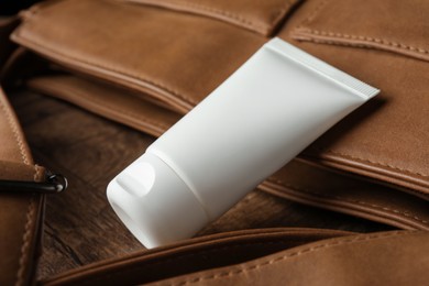 Photo of Tube of moisturizing body cream and leather bag on wooden table, closeup