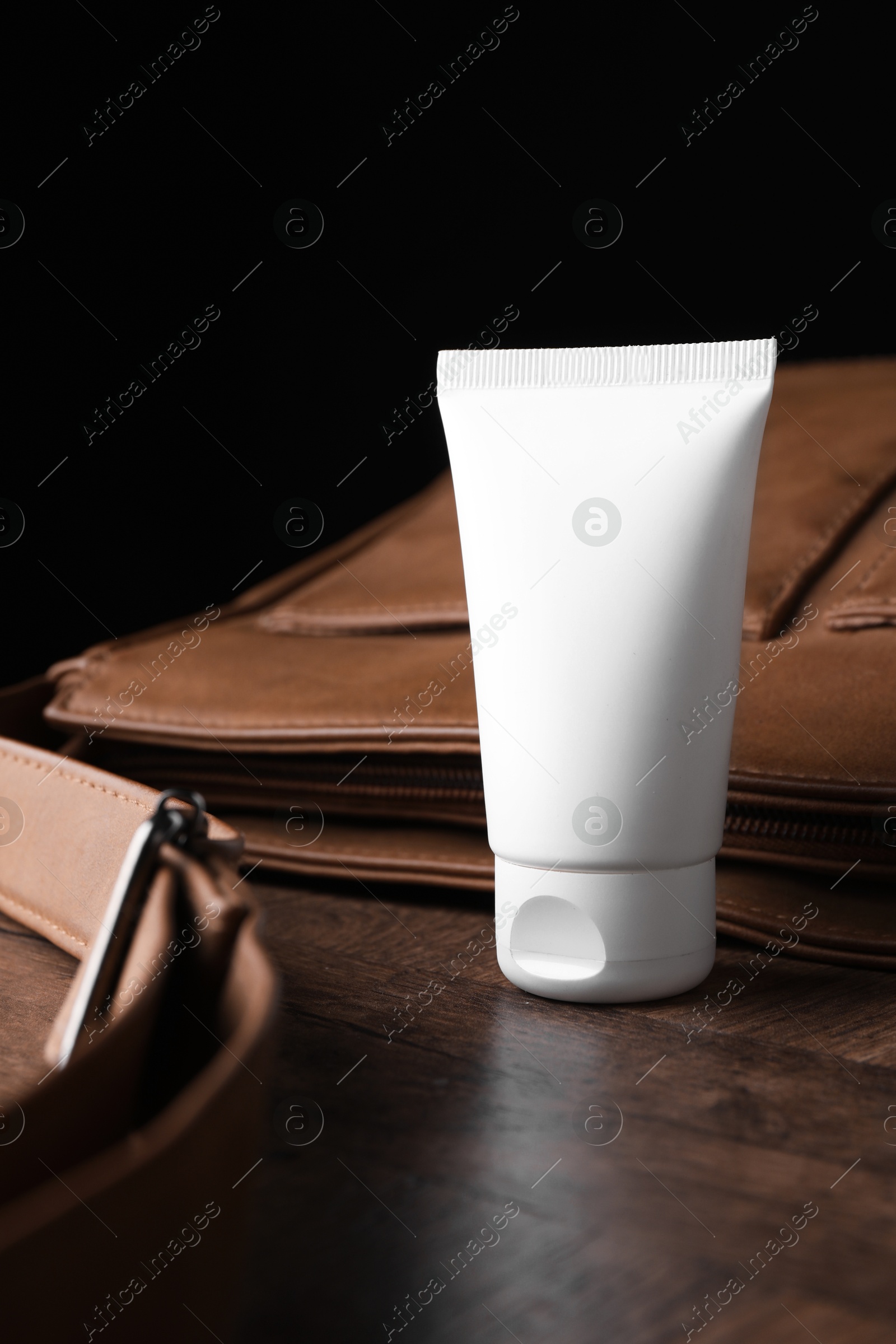 Tube of moisturizing body cream and leather bag on wooden table, closeup Photo of Tube of moisturizing body cream and leather bag on wooden table, closeup
