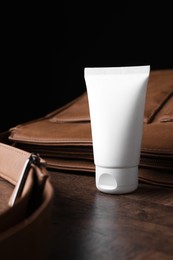 Photo of Tube of moisturizing body cream and leather bag on wooden table, closeup