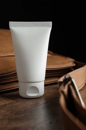 Photo of Tube of moisturizing body cream and leather bag on wooden table, closeup
