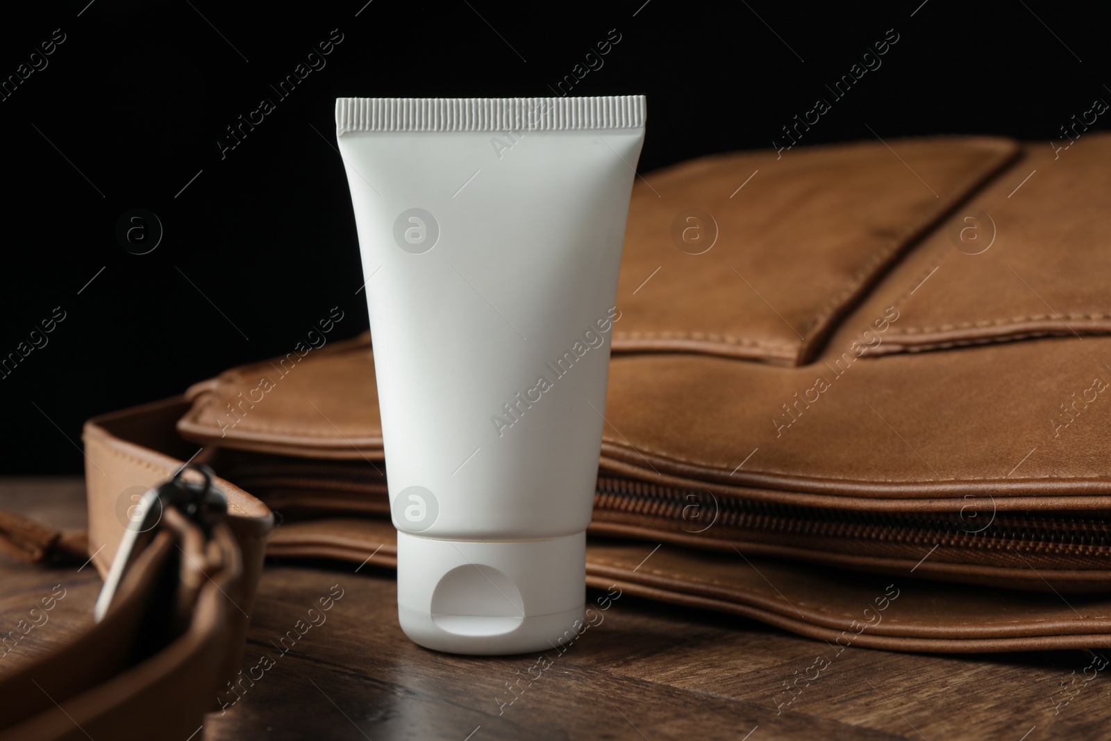 Tube of moisturizing body cream and leather bag on wooden table, closeup Photo of Tube of moisturizing body cream and leather bag on wooden table, closeup