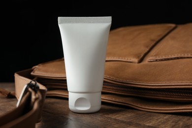 Photo of Tube of moisturizing body cream and leather bag on wooden table, closeup