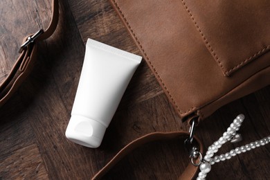Photo of Tube of moisturizing body cream and leather bag on wooden table, flat lay