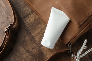 Photo of Tube of moisturizing body cream and leather bag on wooden table, flat lay