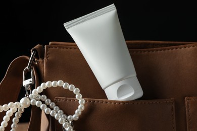 Photo of Tube of moisturizing body cream and leather bag on black background, closeup