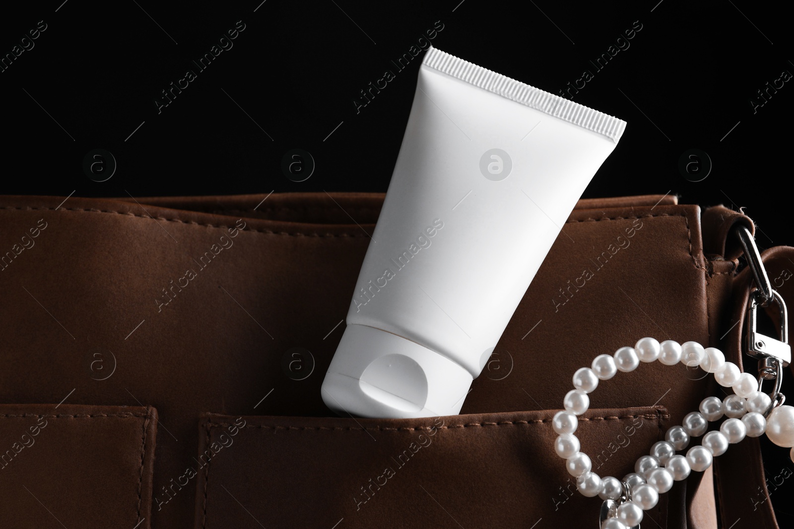 Tube of moisturizing body cream and leather bag on black background, closeup Photo of Tube of moisturizing body cream and leather bag on black background, closeup