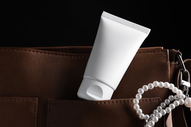 Photo of Tube of moisturizing body cream and leather bag on black background, closeup