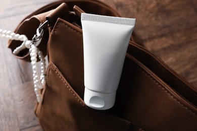 Photo of Tube of moisturizing body cream and leather bag on wooden table, closeup
