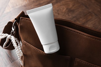 Photo of Tube of moisturizing body cream and leather bag on wooden table, closeup