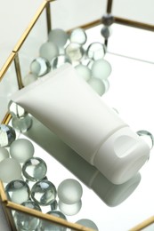 Photo of Tube of moisturizing body cream and glass tray on white table, closeup