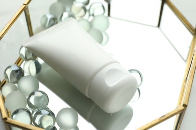Photo of Tube of moisturizing body cream and glass tray on white table, closeup
