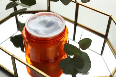 Photo of Jar of moisturizing body cream, leaves and glass tray on white table, closeup