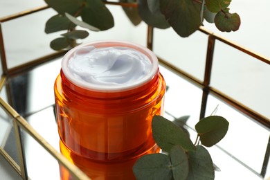 Photo of Jar of moisturizing body cream, leaves and glass tray on white table, closeup