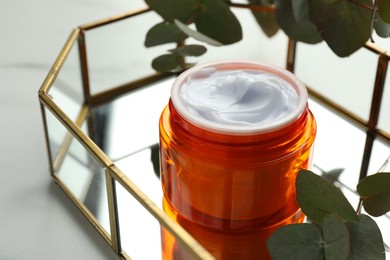 Photo of Jar of moisturizing body cream, leaves and glass tray on white table, closeup