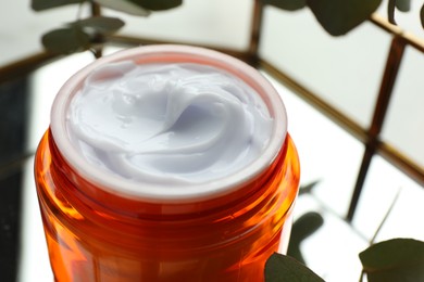 Photo of Jar of moisturizing body cream, leaves and glass tray on white table, closeup