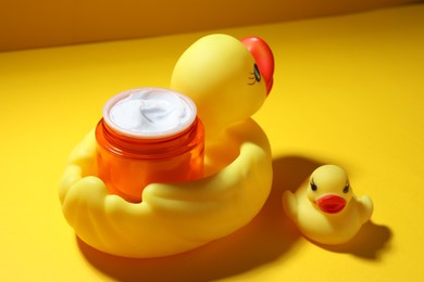 Photo of Jar of moisturizing body cream and rubber ducks on yellow background, closeup