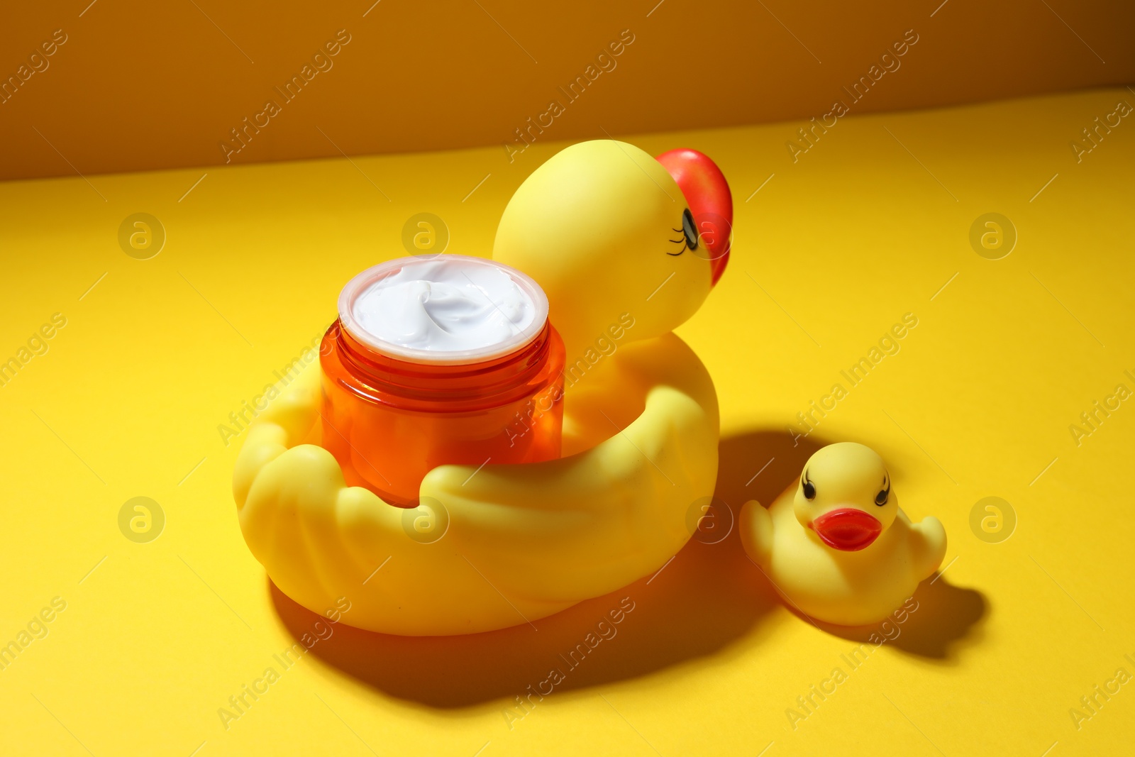 Jar of moisturizing body cream and rubber ducks on yellow background, closeup Photo of Jar of moisturizing body cream and rubber ducks on yellow background, closeup