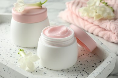 Photo of Jars of moisturizing body cream and flowers on white table, closeup