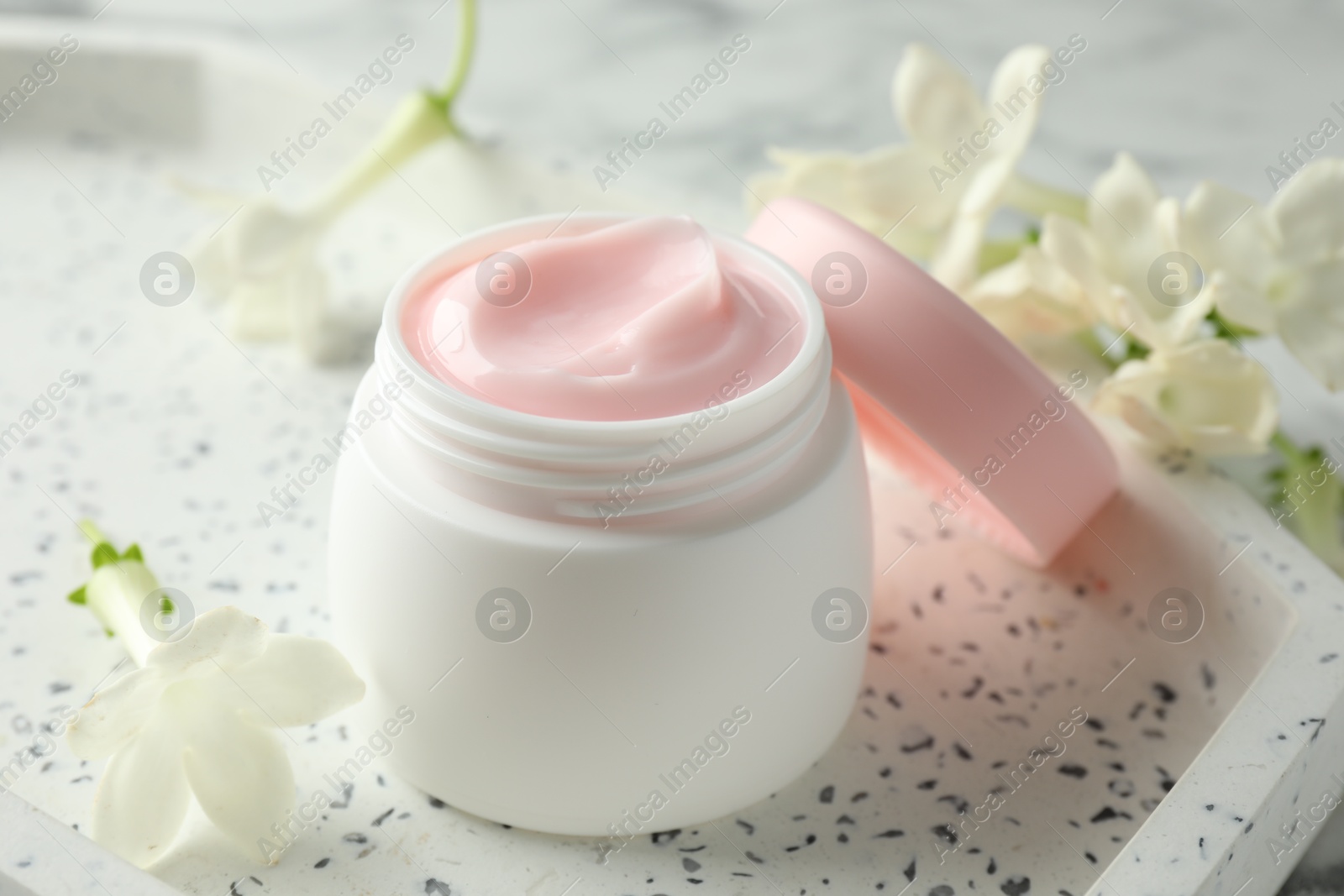 Jar of moisturizing body cream and flowers on white table, closeup Photo of Jar of moisturizing body cream and flowers on white table, closeup