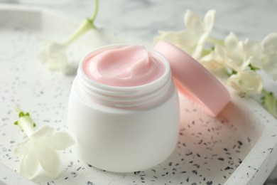 Photo of Jar of moisturizing body cream and flowers on white table, closeup