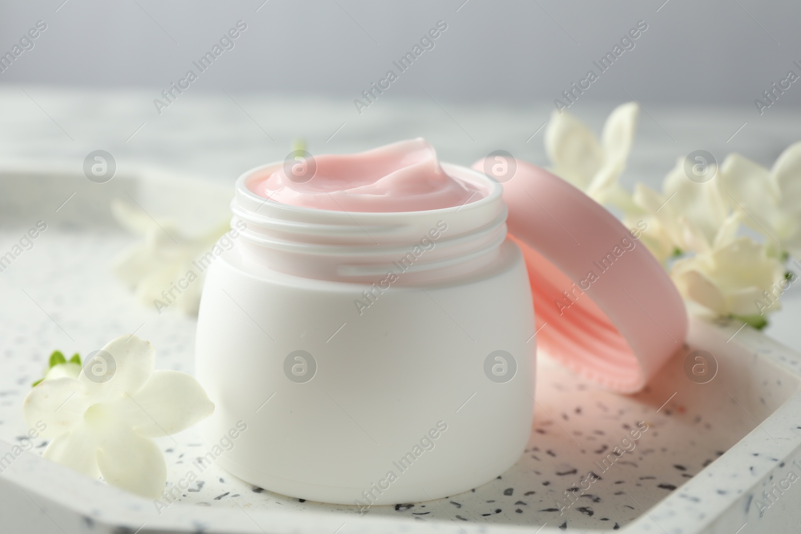Jar of moisturizing body cream and flowers on white table, closeup Photo of Jar of moisturizing body cream and flowers on white table, closeup