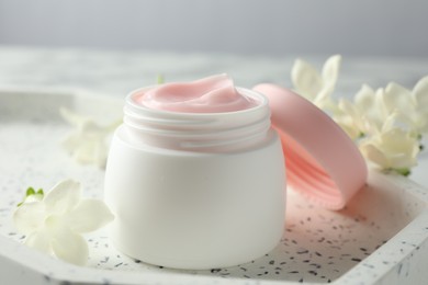 Photo of Jar of moisturizing body cream and flowers on white table, closeup