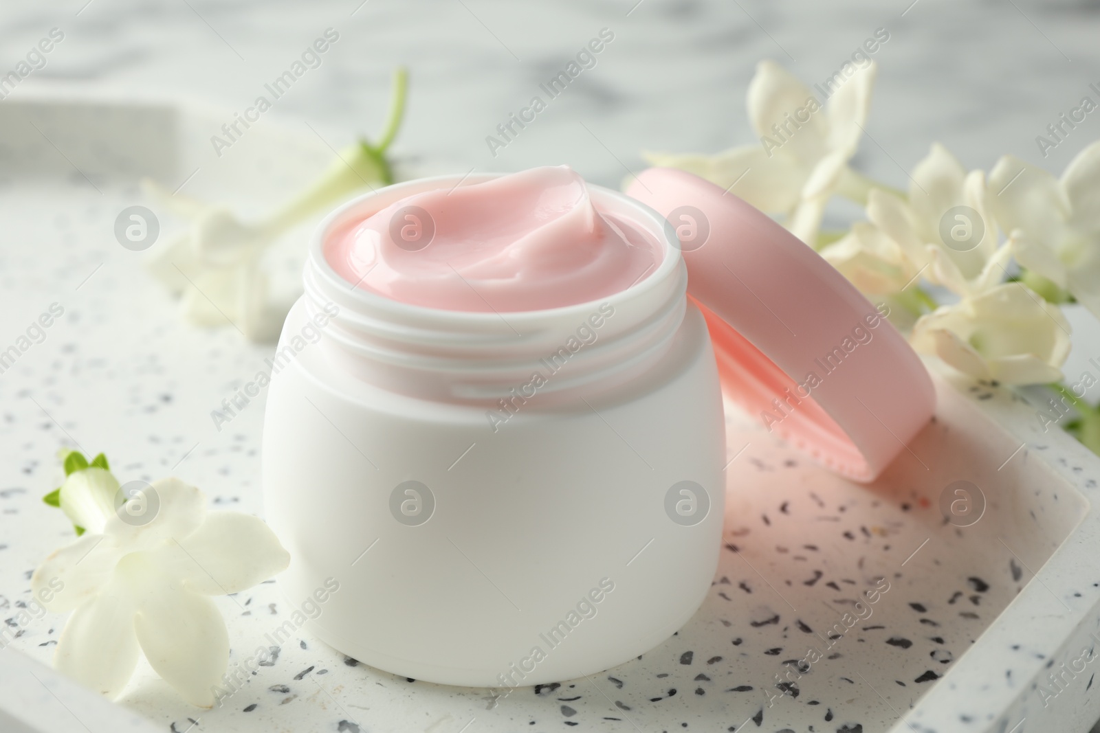 Jar of moisturizing body cream and flowers on white table, closeup Photo of Jar of moisturizing body cream and flowers on white table, closeup