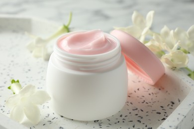 Photo of Jar of moisturizing body cream and flowers on white table, closeup