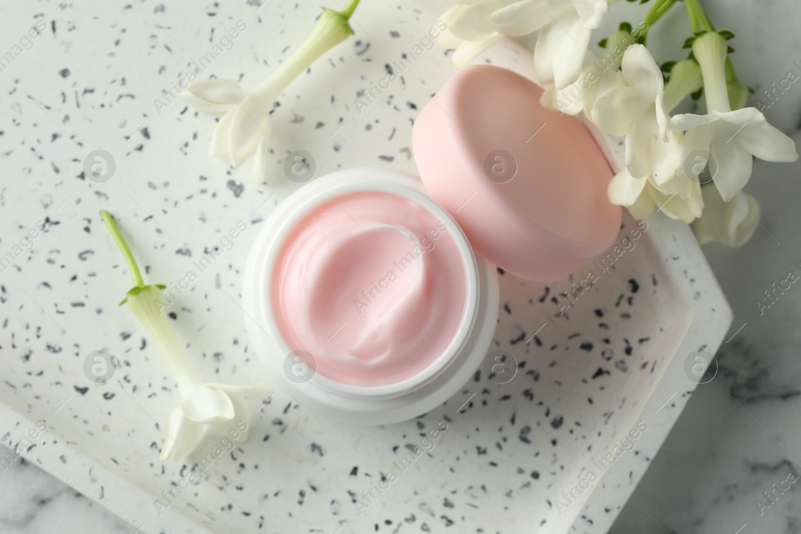 Jar of moisturizing body cream and flowers on white marble table, flat lay Photo of Jar of moisturizing body cream and flowers on white marble table, flat lay