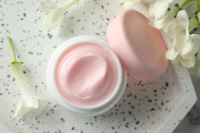 Photo of Jar of moisturizing body cream and flowers on white marble table, flat lay