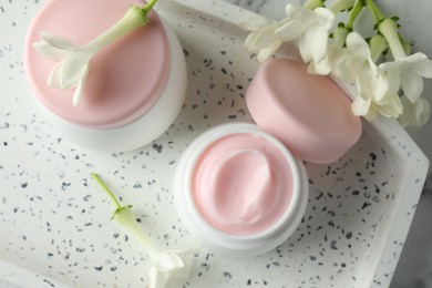 Photo of Jars of moisturizing body cream and flowers on white marble table, flat lay