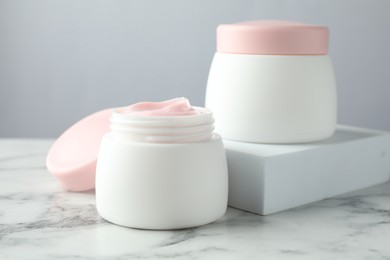 Photo of Jars of moisturizing body cream on white marble table, closeup