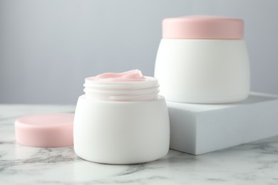 Photo of Jars of moisturizing body cream on white marble table, closeup