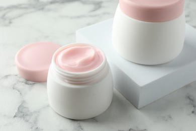 Photo of Jars of moisturizing body cream on white marble table, closeup