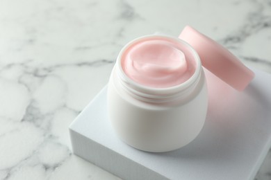 Photo of Jar of moisturizing body cream on white marble table, closeup. Space for text