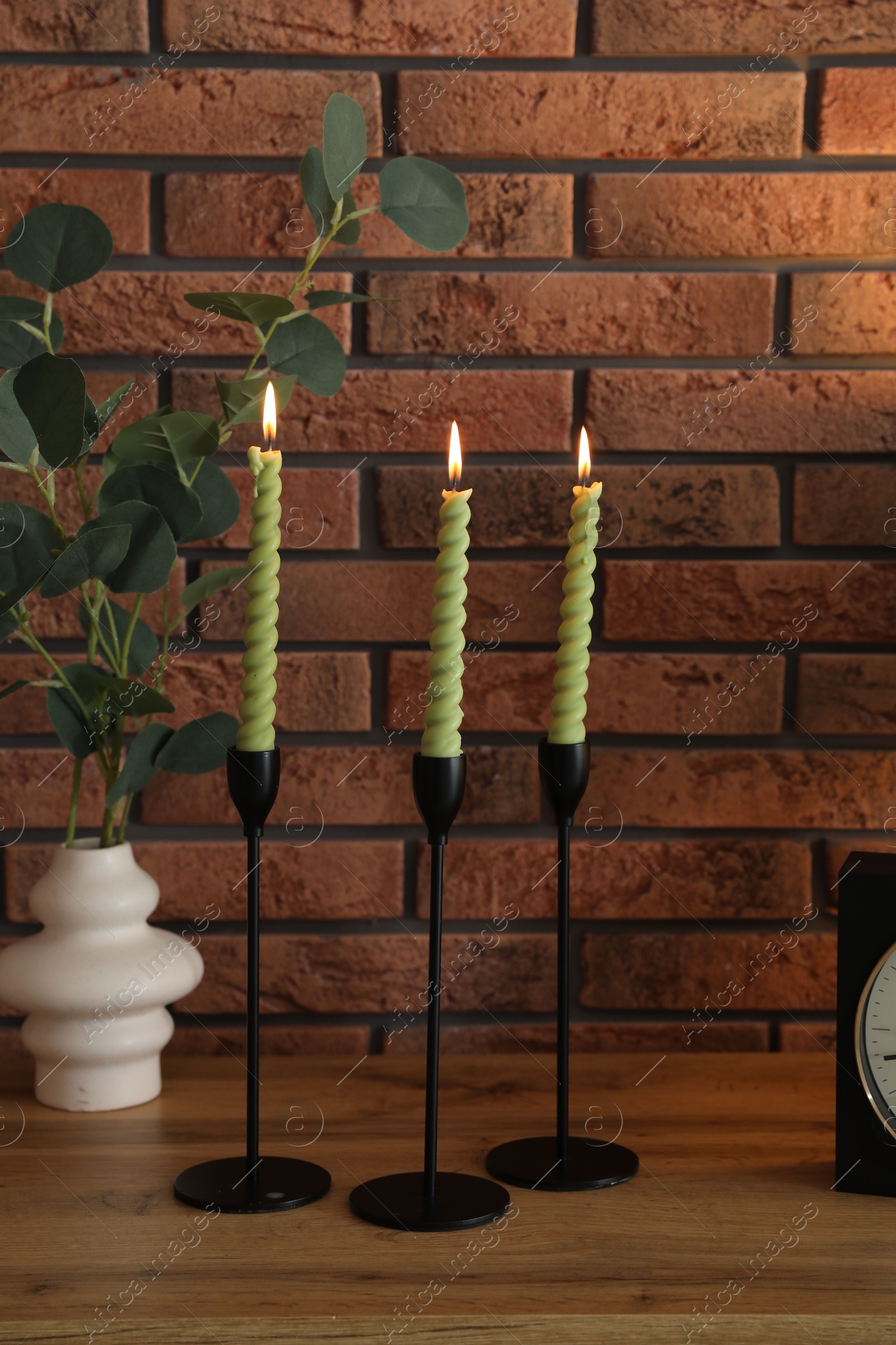 Candlesticks with burning candles on table near brick wall Photo of Candlesticks with burning candles on table near brick wall